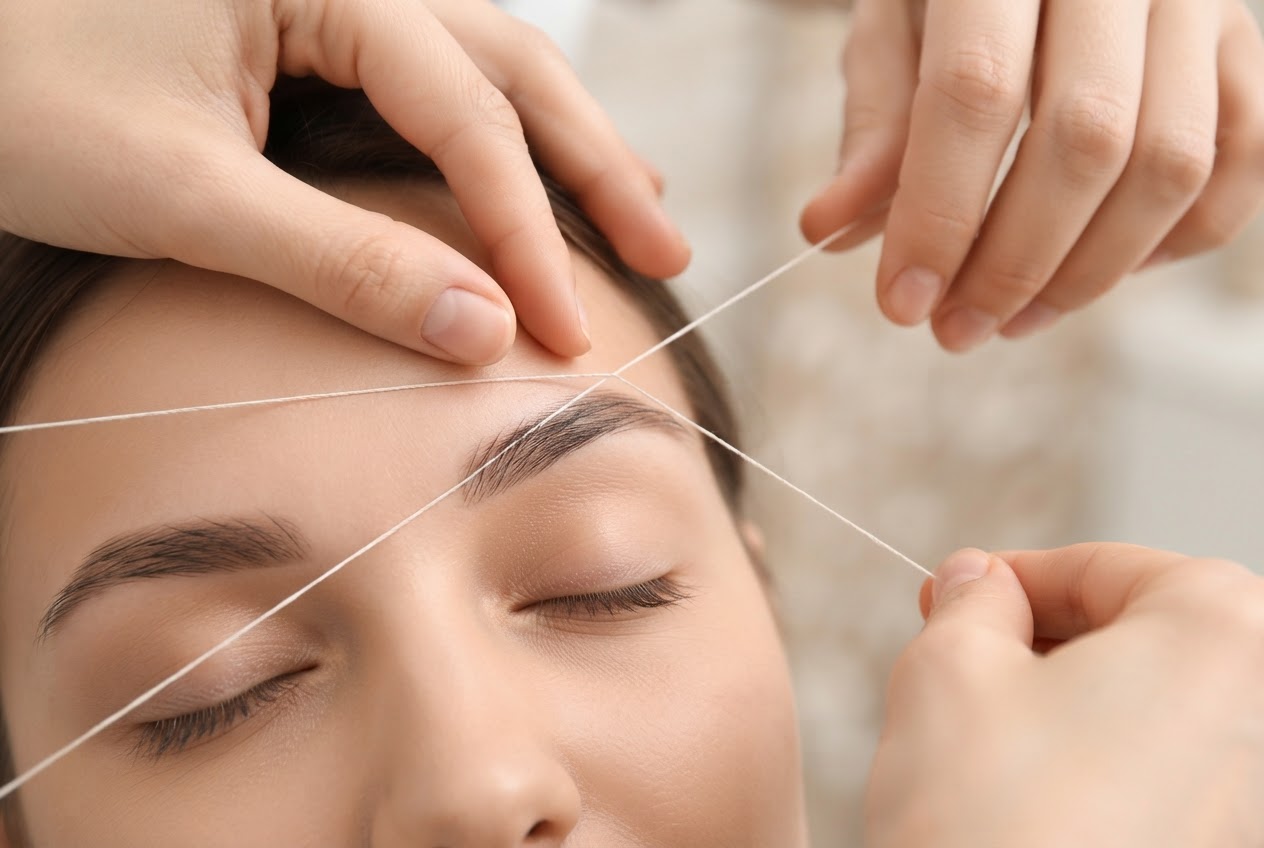 A beautician's hands guide the thread along a client's eyebrow, creating a crisp, natural brow line.