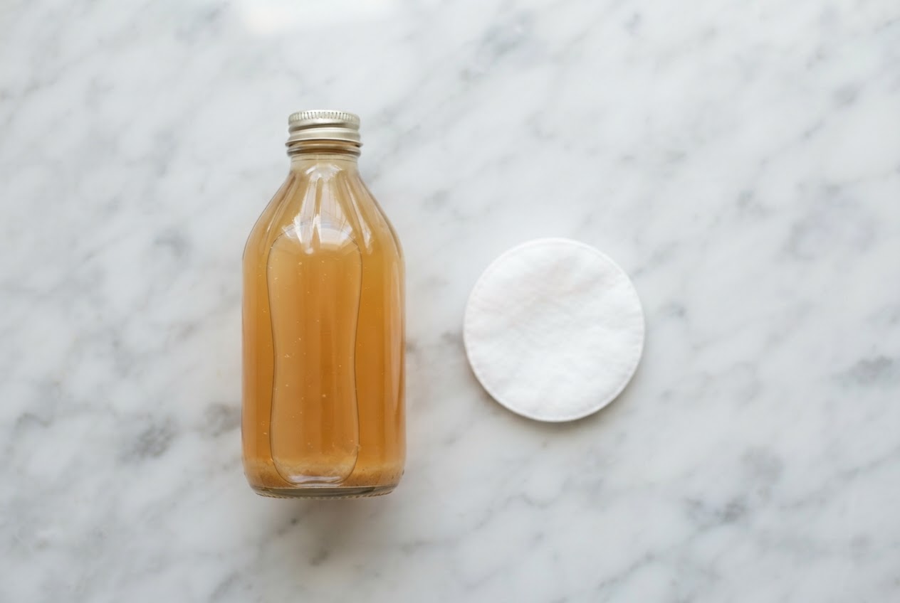 A bottle of apple cider vinegar and a cotton pad on a bathroom counter.