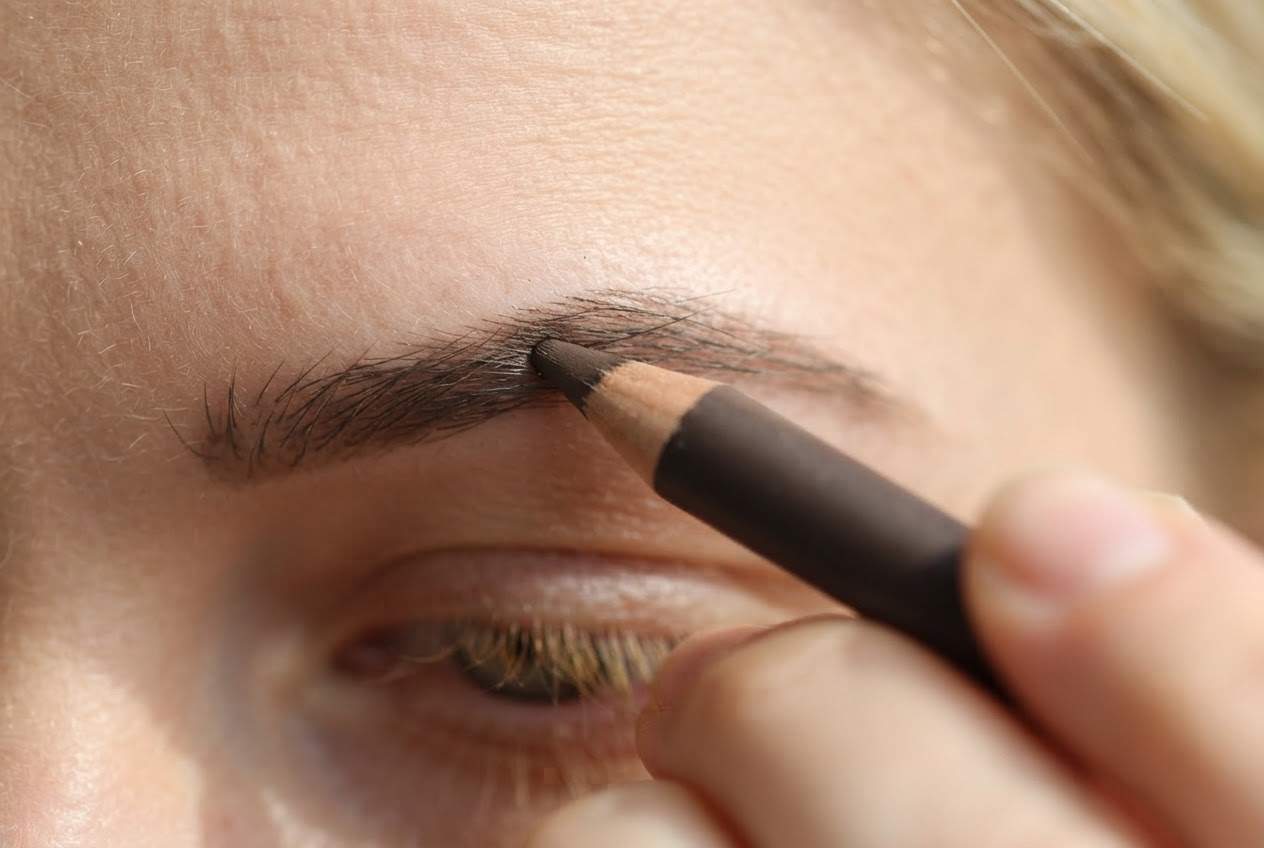 Close-up of filling in sparse eyebrow hairs with a brow pencil using short, light strokes.