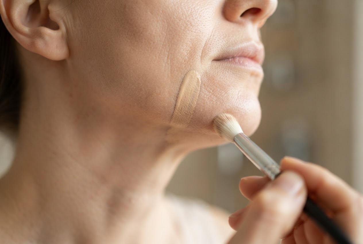 A person swatching foundation on their jawline, comparing the shade to their neck in daylight.