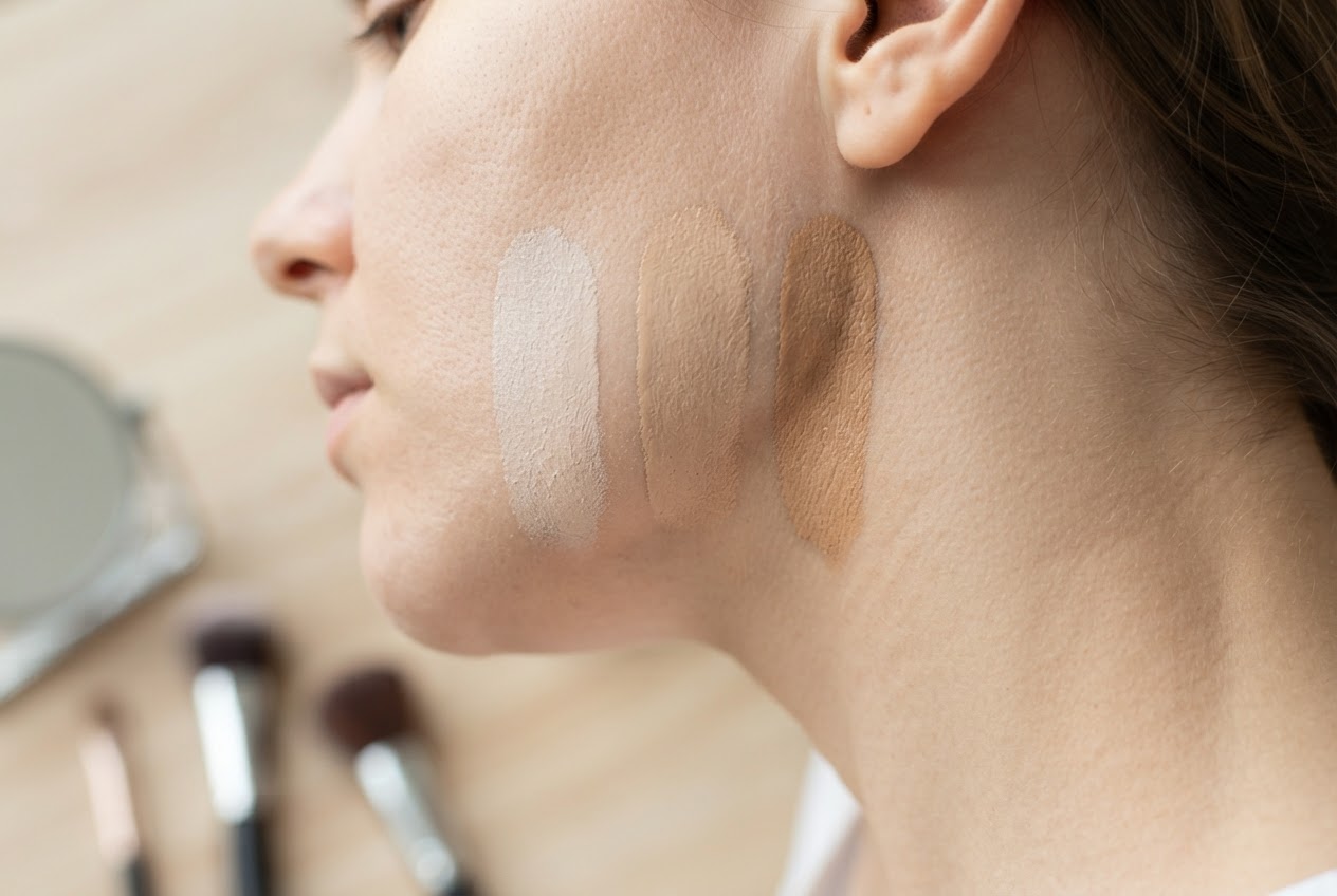 A close-up of a jawline with three foundation swatches in different shades, showing how to match the skin tone.