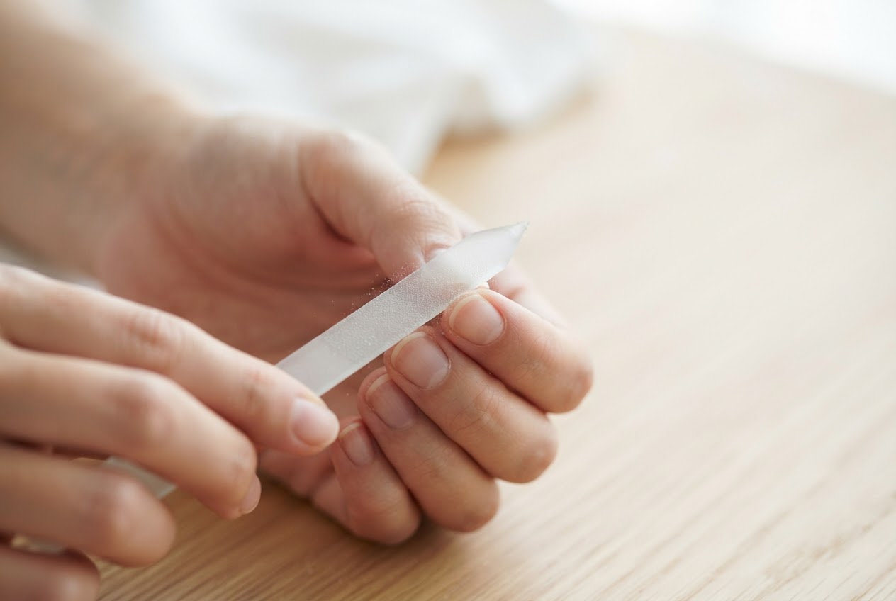 Hand, die einen Nagel in einer Richtung mit einer Glasfeile feilt