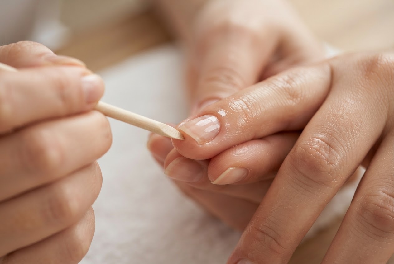 Hand, bei der die Nagelhaut sanft mit einem Holzstäbchen zurückgeschoben wird