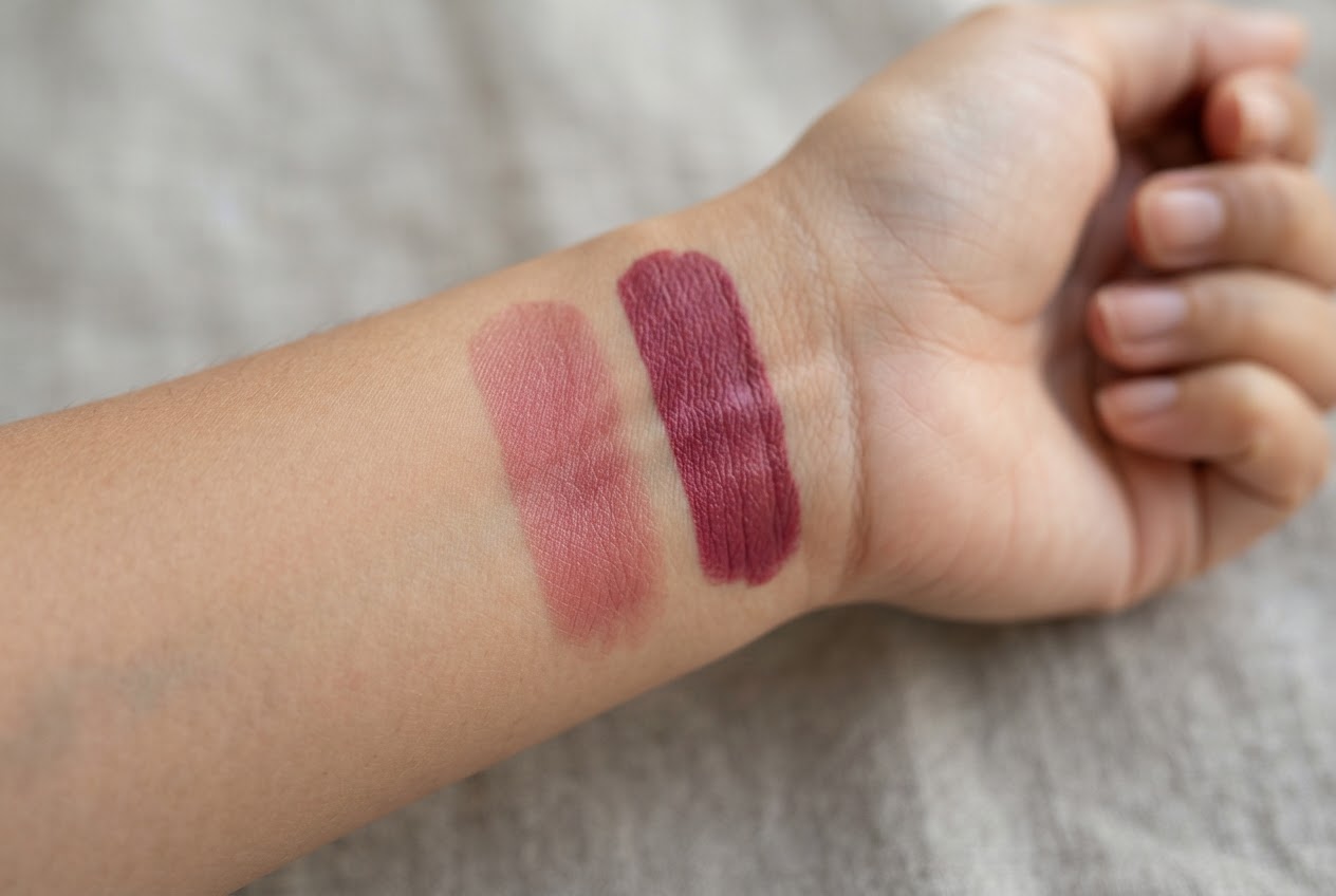 A close-up of a hand with a swatch of a sheer lipstick, showing the skin texture through the product, and another swatch with full coverage.