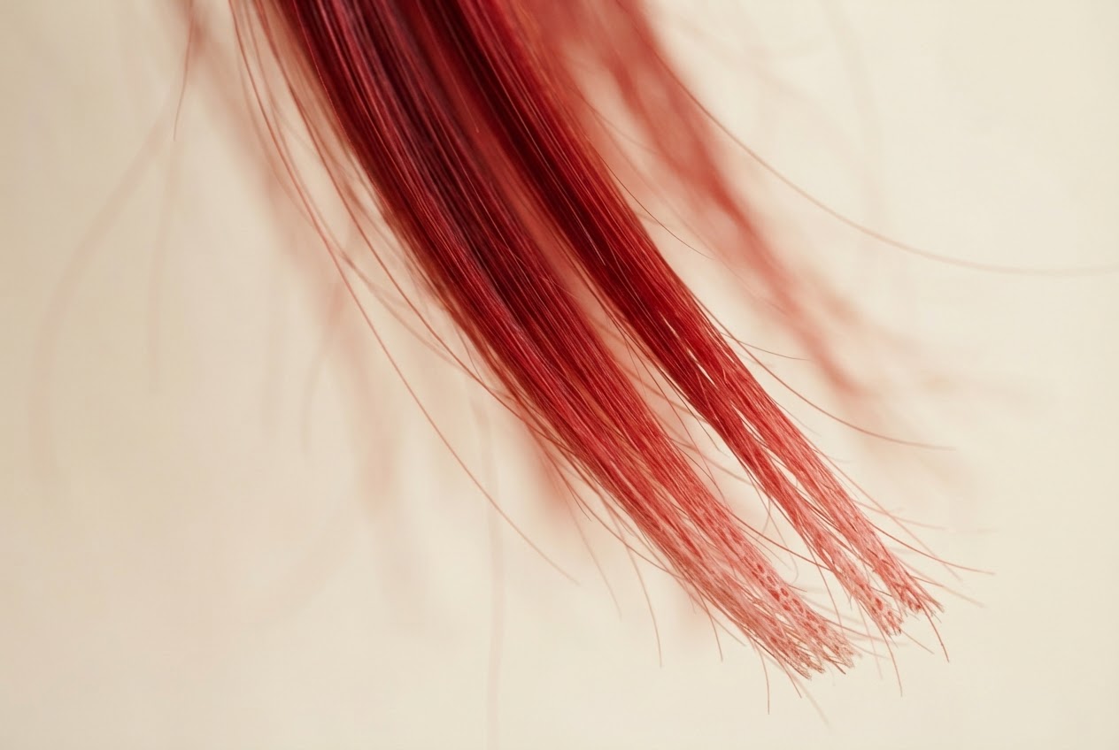 Macro photo of red hair strands with slightly faded ends, showing color difference along the shaft.