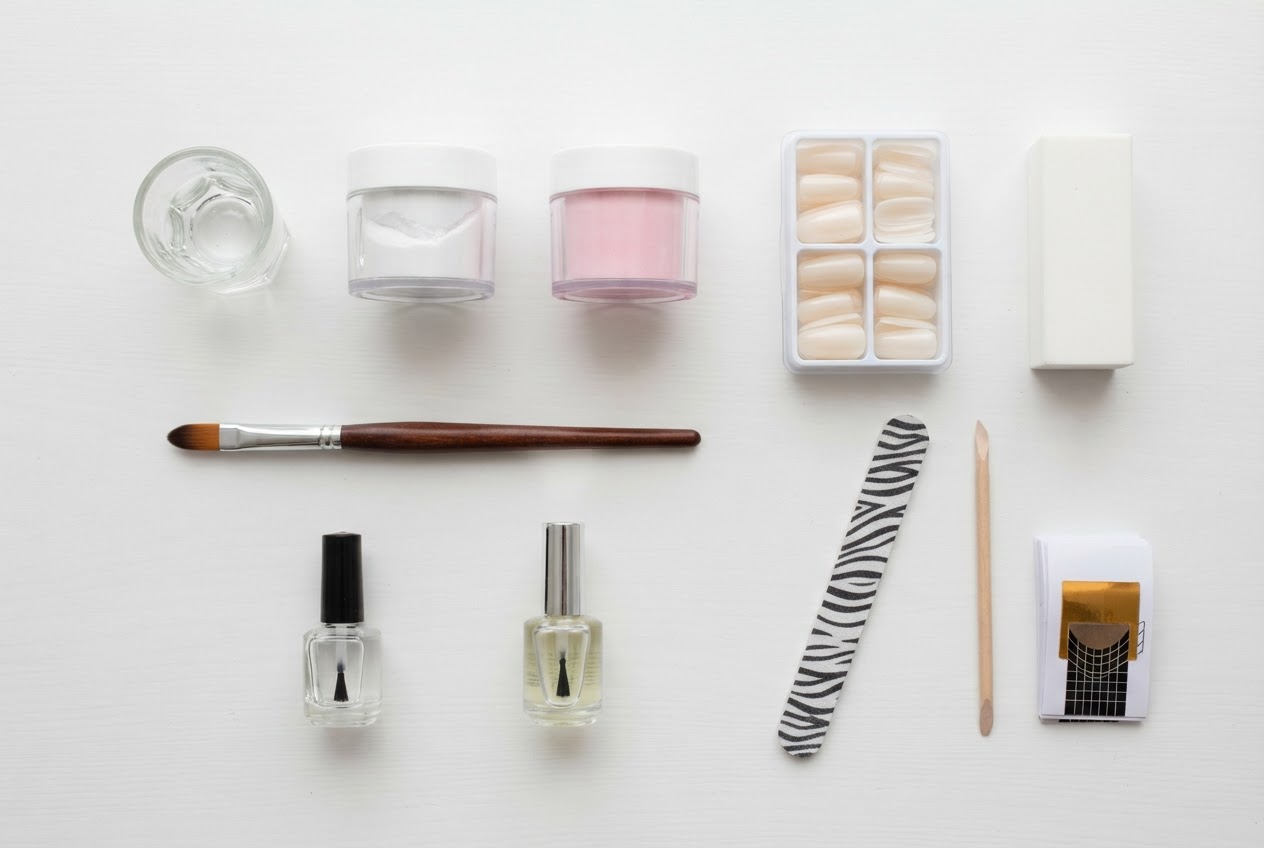 Flat lay of acrylic nail supplies: powder, liquid, brush, tips, file, buffer, primer.