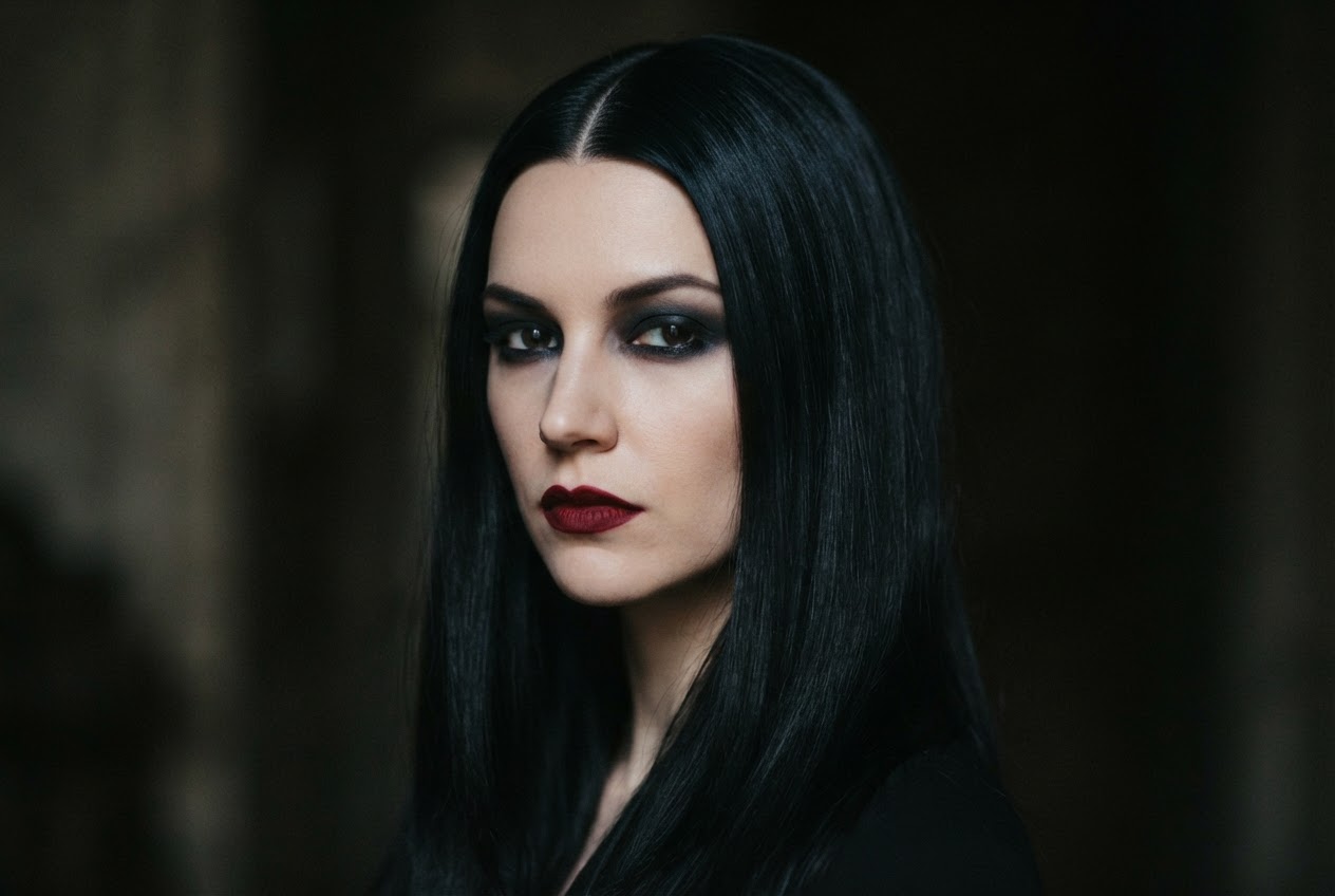 Woman with jet black hair in a sleek middle part, dark smoky eye shadow, and deep red lipstick, moody lighting.