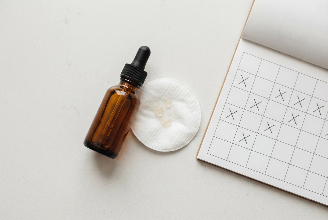 A flat lay of an AHA serum bottle, a cotton pad with a few drops, and a small calendar marking days with an X, indicating alternate-day use.
