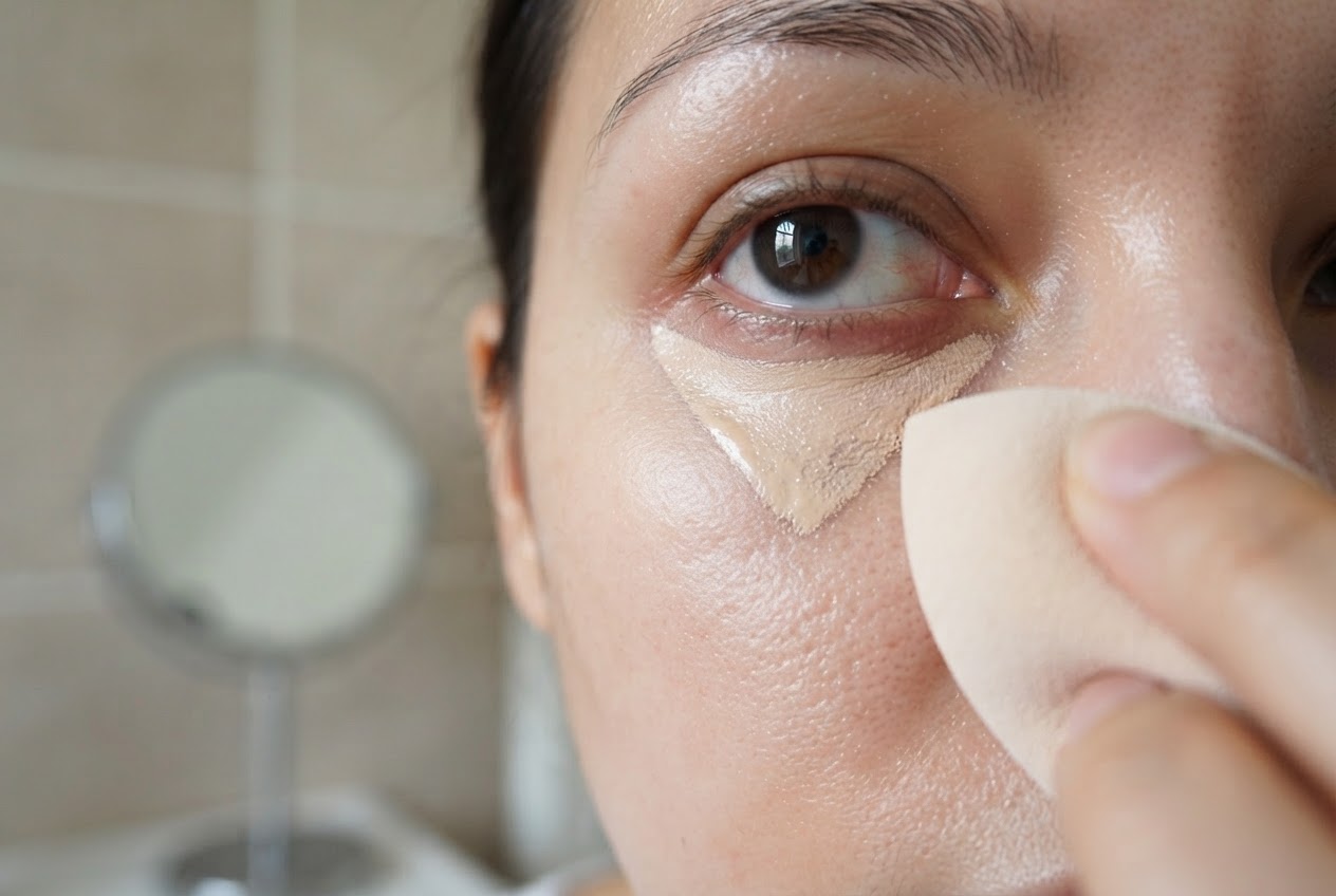 Close-up of the under-eye area with concealer applied in a triangle shape, being blended outward.