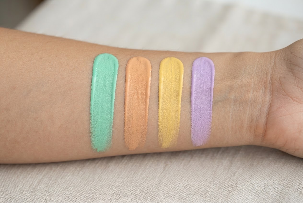 Unterarm mit vier nebeneinander aufgetragenen Farbkorrektur-Swatches in Grün, Pfirsich, Gelb und Lavendel