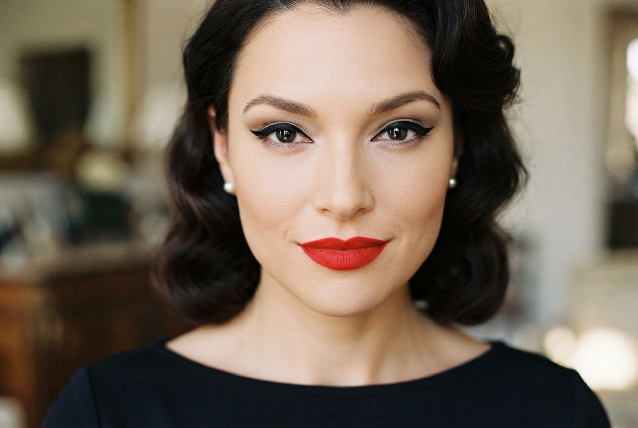 Porträt einer Frau mit klassischem 50er-Jahre-Make-up: rote Lippen, Winged Eyeliner und ebenmäßiger Teint.