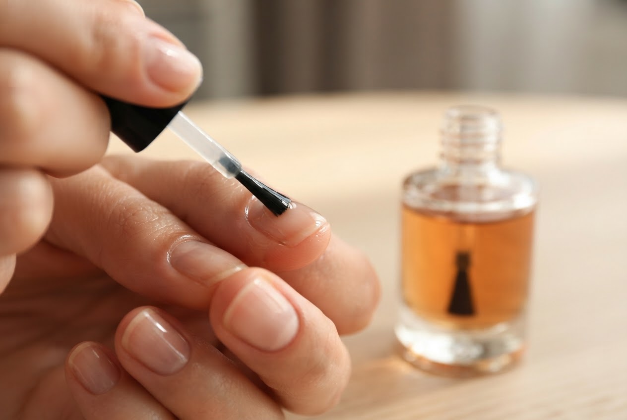 Eine Hand trägt mit einem Pinsel Nagelöl auf die Nagelhaut auf.