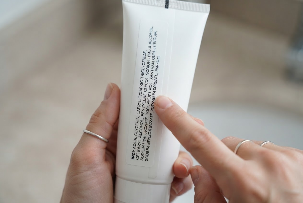 Eine Hand hält eine Kosmetiktube, auf deren Rückseite die INCI-Liste mit Inhaltsstoffen zu sehen ist.