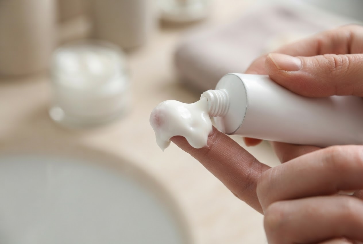 A hand squeezing a large blob of cream from a tube onto a fingertip.