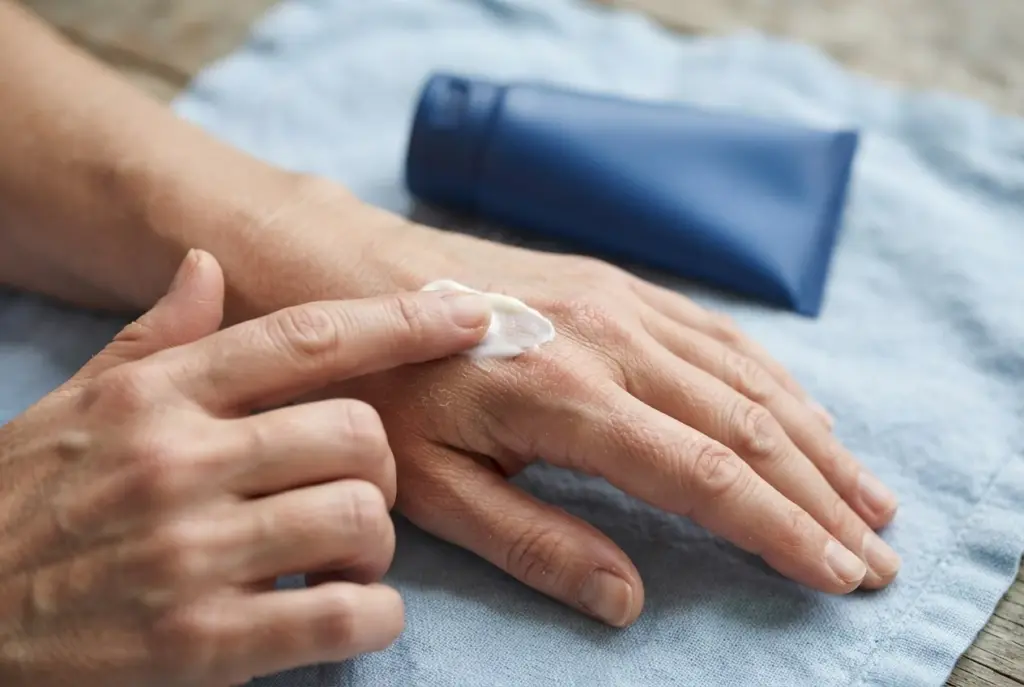 Nahaufnahme trockener Fingerknöchel mit einer kleinen Menge weißer Pflegecreme.