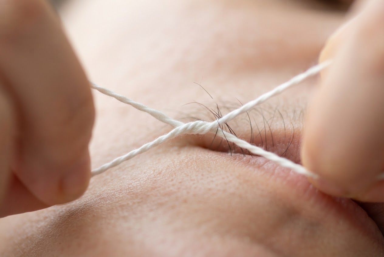 Close-up of hands forming the twisted cotton thread in a figure-eight loop, with a few hairs being pulled out from the skin.