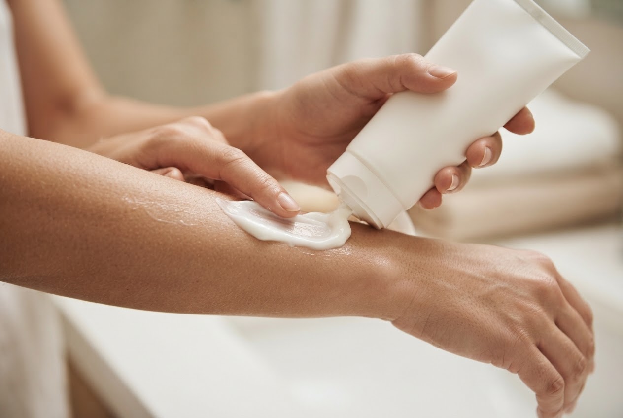 Hand drückt reichhaltige Bodylotion aus einer unbeschrifteten Tube auf die Haut