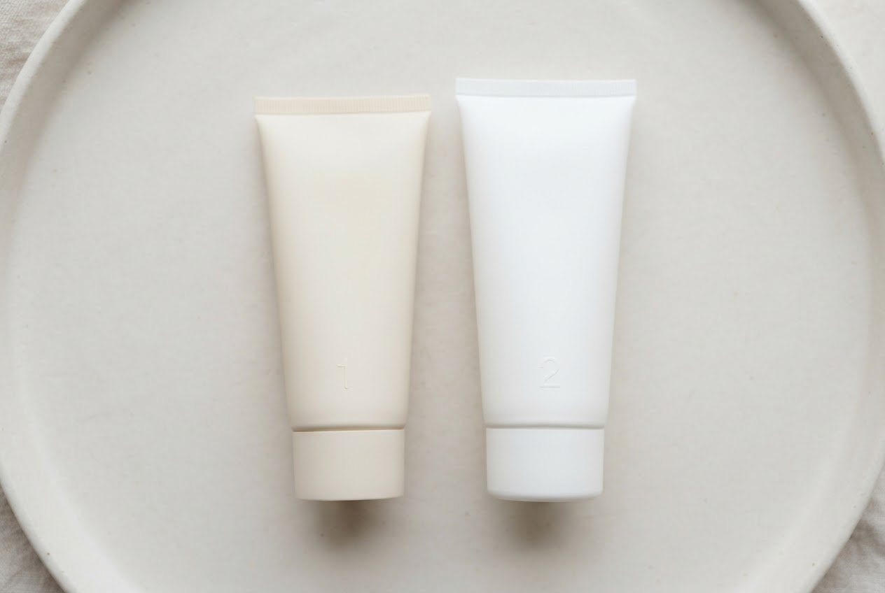 Zwei unbeschriftete Pflegeprodukte nebeneinander: Peeling-Creme und Bodylotion, in der richtigen Reihenfolge angeordnet